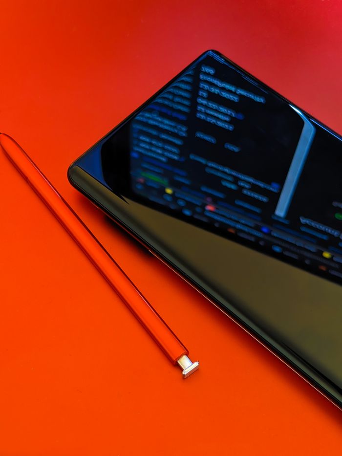 A close-up shot of a smartphone with a stylus resting on a vivid red surface, highlighting contemporary technology.